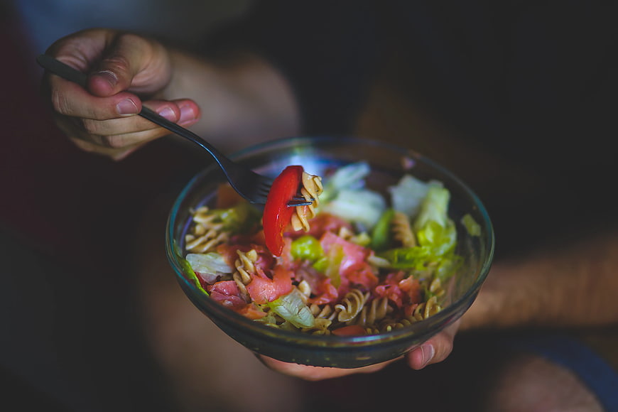 Close-up of hands eating healthy pasta salad with vegetables