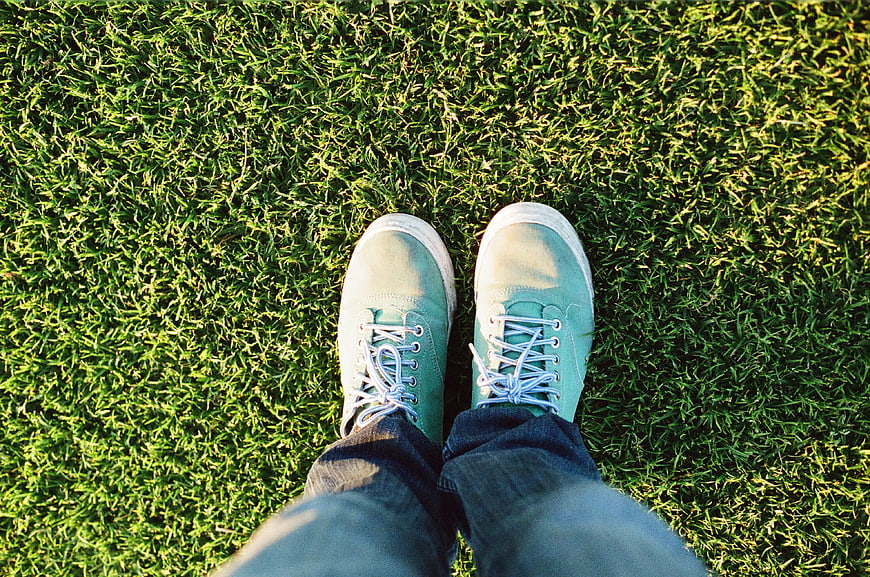 First-person view of blue sneakers on green grass