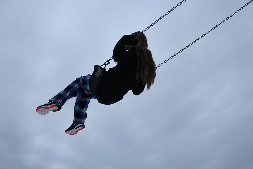 Child swinging high against cloudy sky