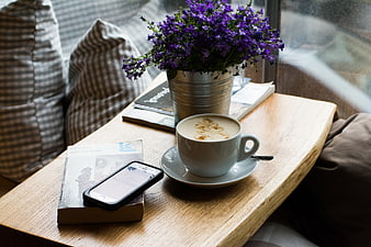 Cozy coffee cup with latte art, purple flowers, and books on wooden table