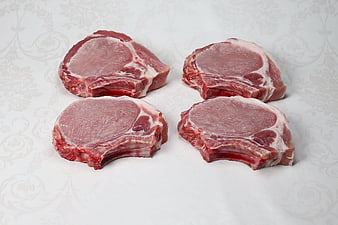 Four raw pork chops on white patterned background