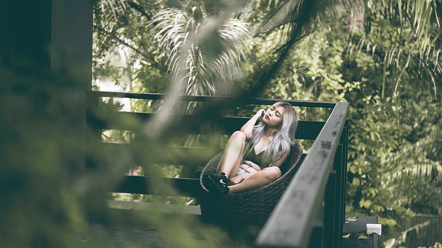 Relaxed woman with silver hair resting on a balcony surrounded by lush greenery