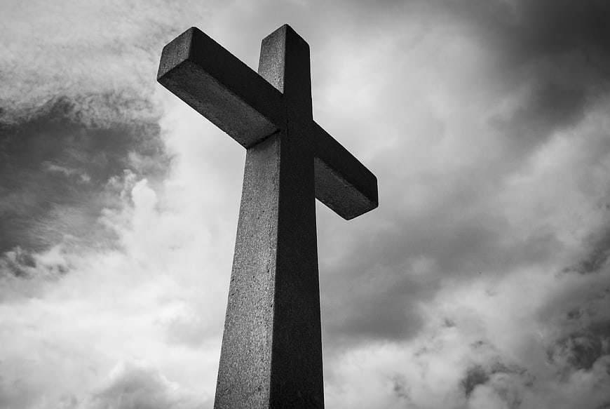 Black and white stone cross against dramatic cloudy sky