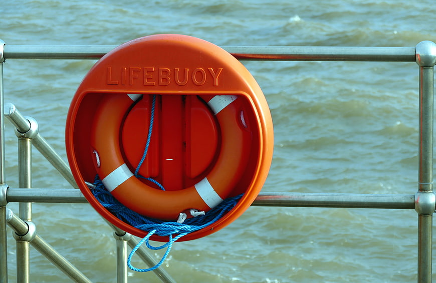 Orange Lifebuoy on Metal Railing by Water