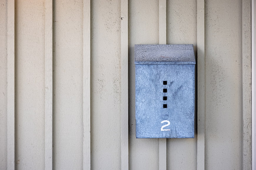 Blue metal mailbox with number two on beige siding
