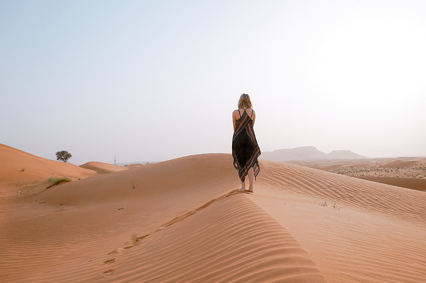 Woman in Black Dress Walking on Sand Dunes in Desert