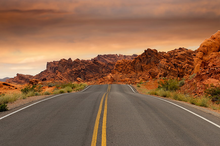 Desert highway winding through red rock formations at sunset