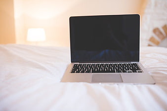 Silver laptop on white bed sheets with blurred background