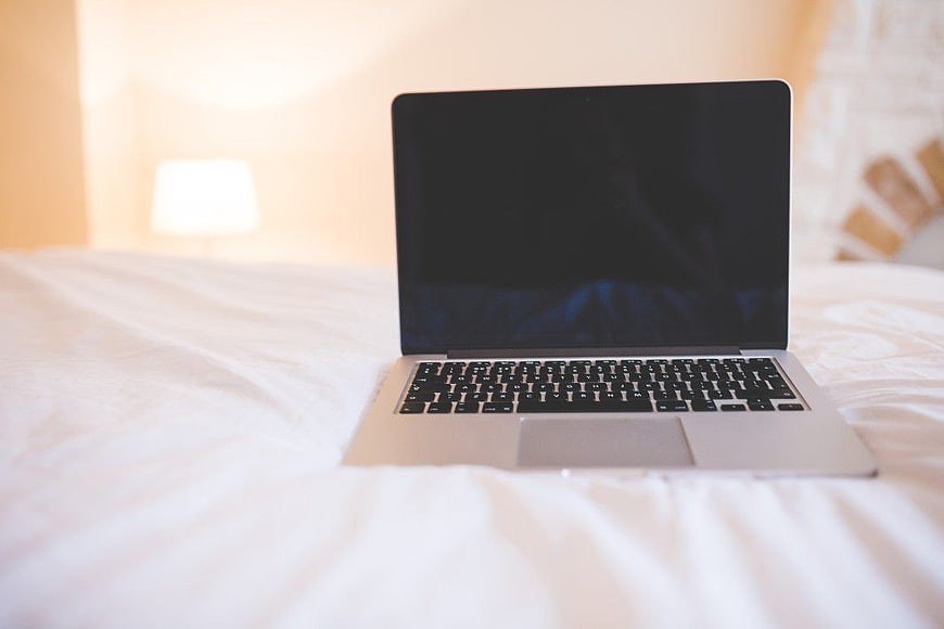 Silver laptop on white bed sheets with blurred background