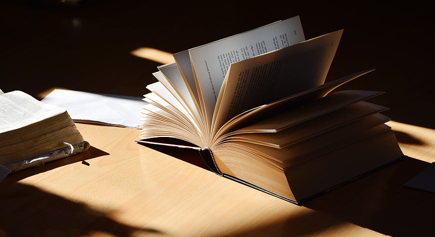Open Book With Flipping Pages in Warm Sunlight on Wooden Table