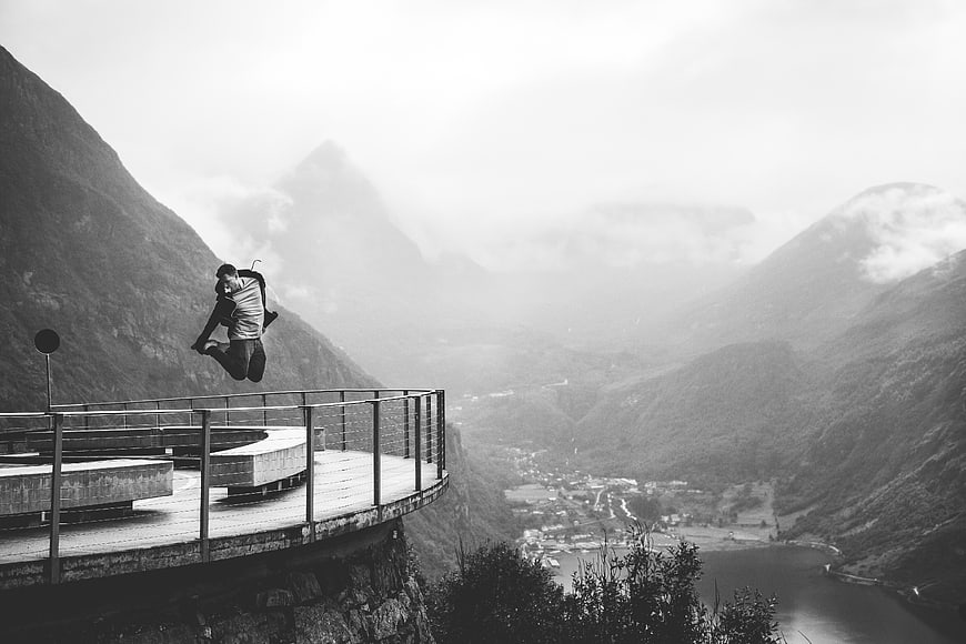 Man jumping on cliffside lookout with mountain landscape