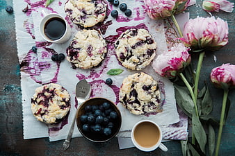 Overhead view of blueberry scones, coffee, and pink peonies on rustic table