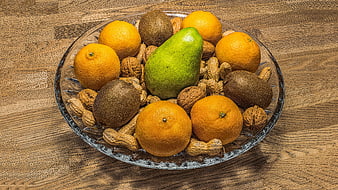 Glass bowl of fresh oranges, kiwi, pear, and nuts on wood