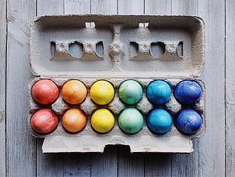 Rainbow colored Easter eggs in a cardboard carton on wood