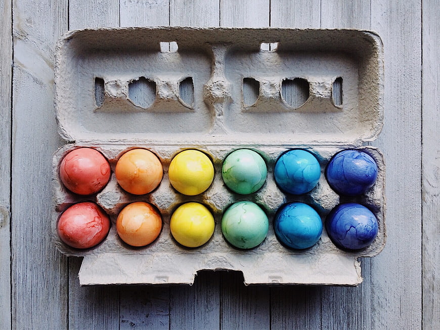 Rainbow colored Easter eggs in a cardboard carton on wood