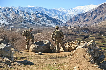 Two soldiers in camouflage gear overlooking a mountainous valley