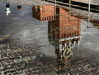 Upside down clock tower reflection in cobblestone puddle