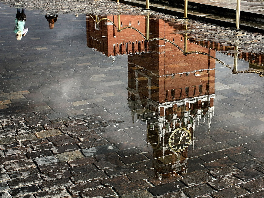 Upside down clock tower reflection in cobblestone puddle