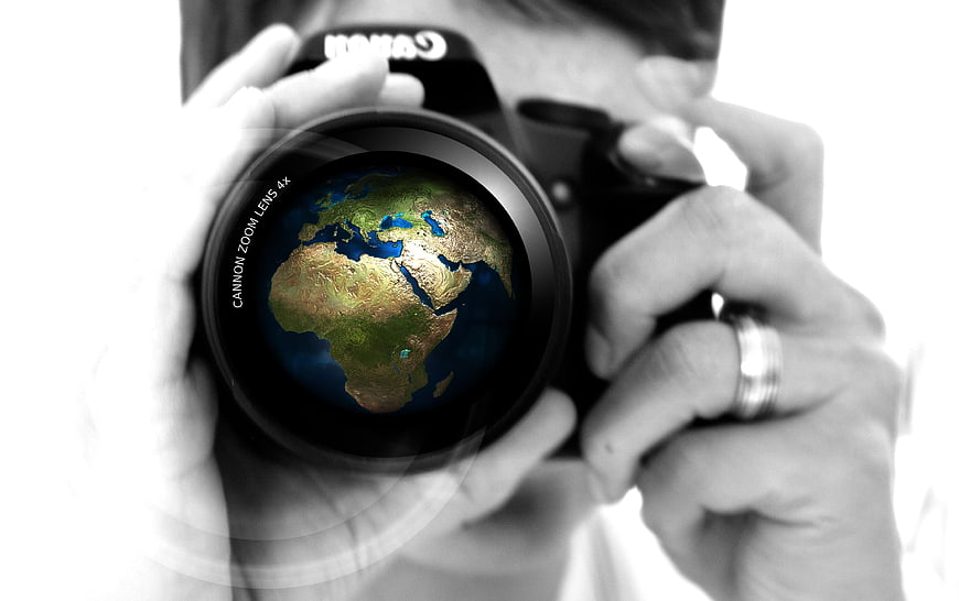 Photographer holding camera with globe reflection in lens