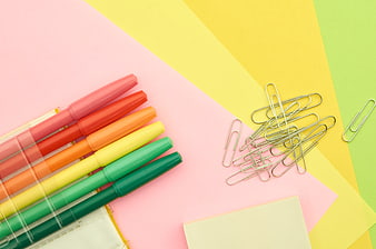 Colorful markers and paper clips on pastel background