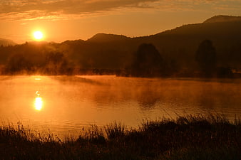 Golden sunrise over misty river with silhouetted hills