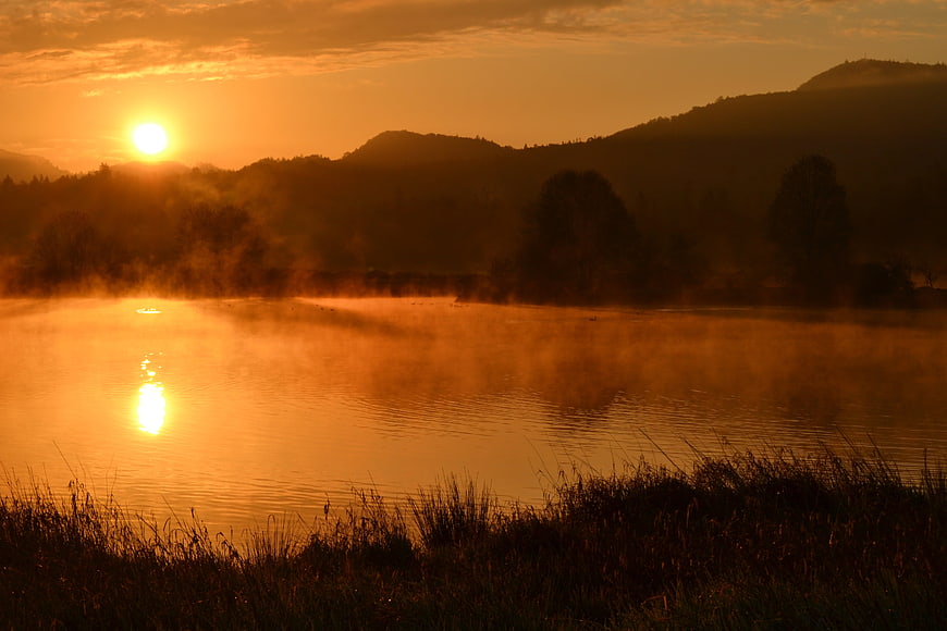 Golden sunrise over misty river with silhouetted hills