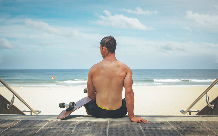 Muscular Man Sitting on Beach Steps with Skateboard