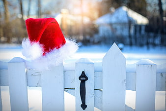 Red Santa hat on white picket fence in snowy winter landscape
