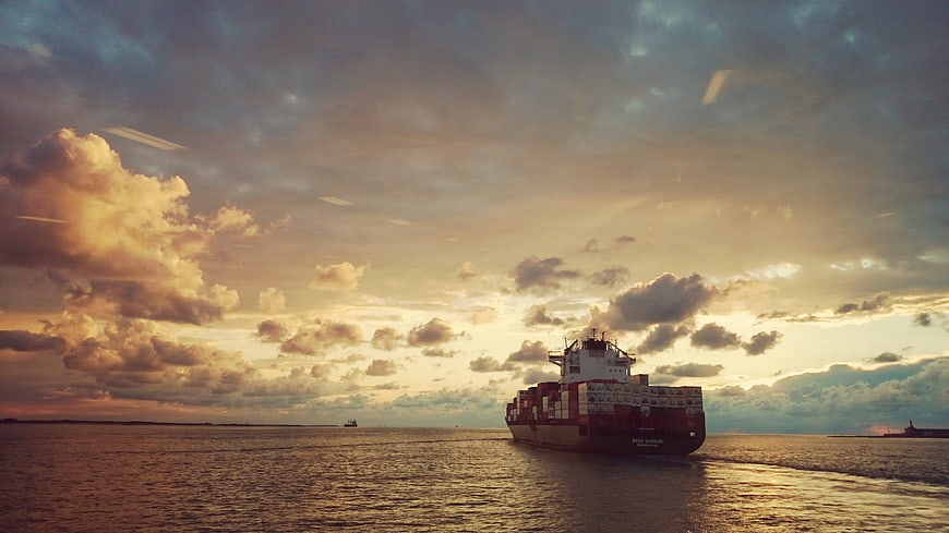 Cargo Ship Sailing on Ocean at Sunset with Dramatic Clouds