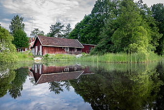 Red wooden boathouse reflecting in calm lake water
