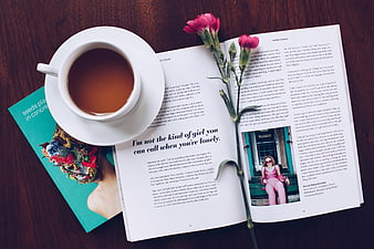 Flat lay of coffee cup, open magazine, and pink flowers on wood