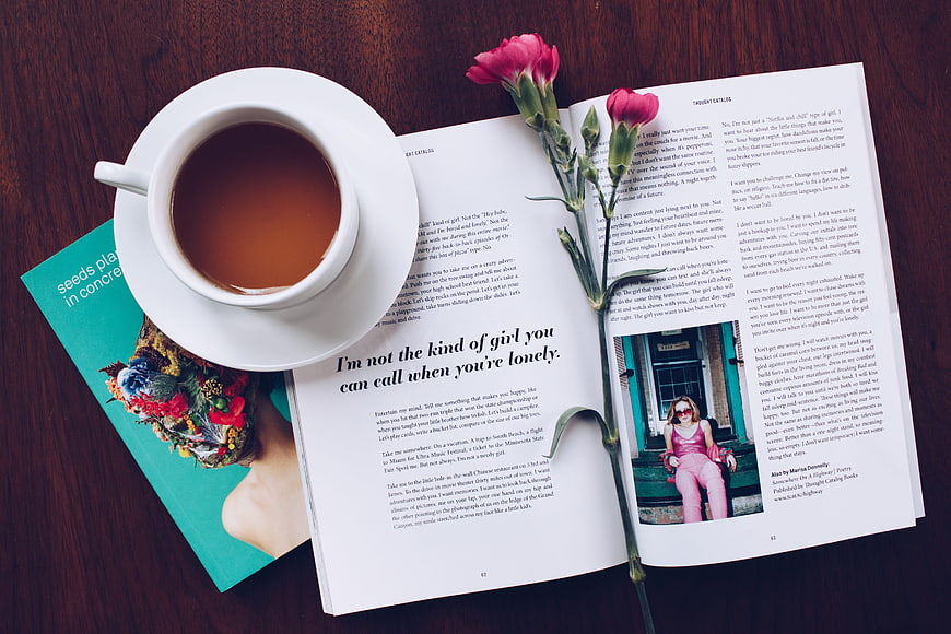 Flat lay of coffee cup, open magazine, and pink flowers on wood