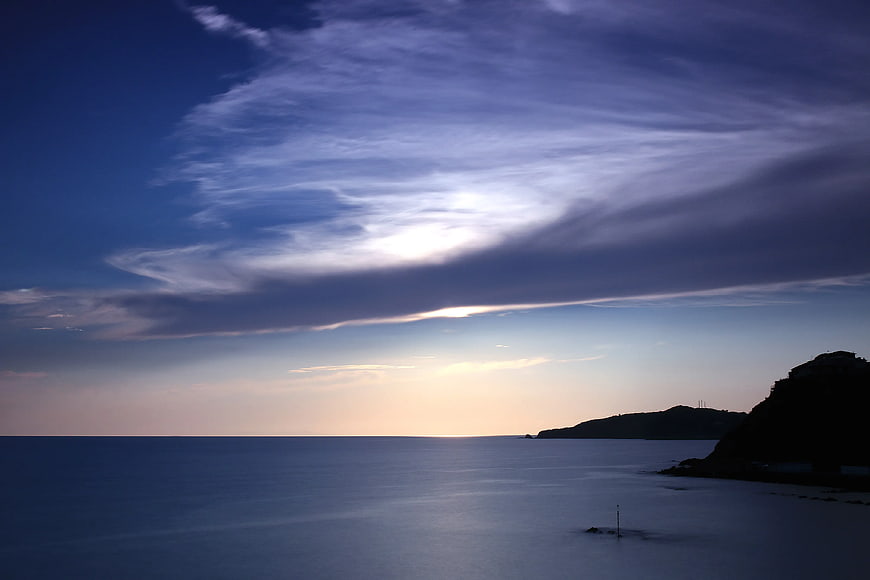 Serene Coastal Sunset with Silhouetted Cliffs and Smooth Ocean