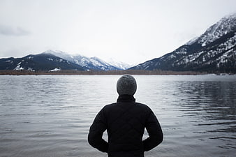 Man in winter jacket looking at snowy mountain lake