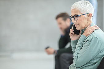 Senior woman holding shoulder in pain while talking on phone