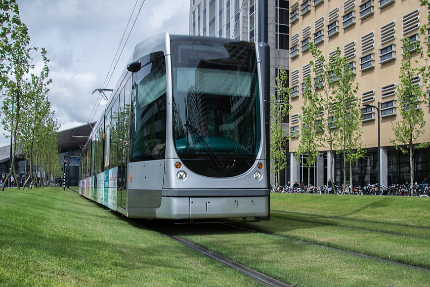 Modern silver tram on grass tracks in urban city