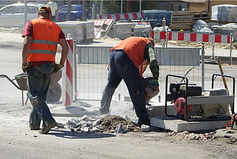 Two construction workers performing road repair on a street
