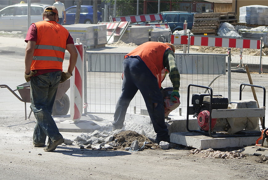 Two construction workers performing road repair on a street
