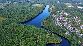 Aerial view of winding river through lush forest and suburban homes