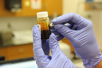 Gloved Hands Labeling Amber Vial In Laboratory