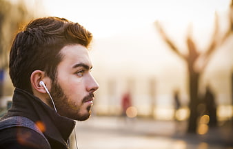 Young man in profile with white earbuds and beard