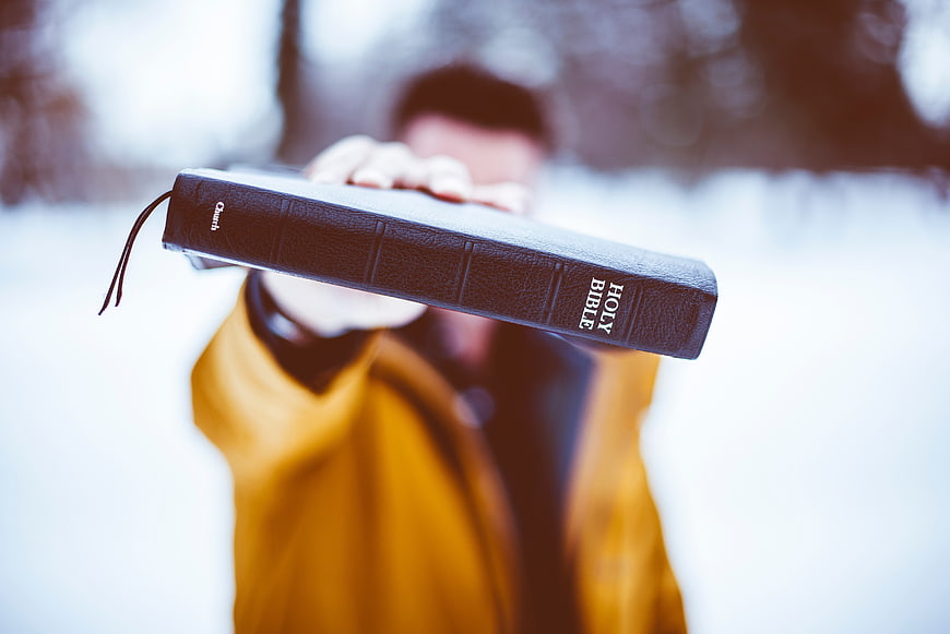 Man Holding Holy Bible in Snowy Winter Landscape