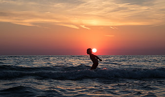 Silhouette of Boy Playing in Ocean Waves at Sunset