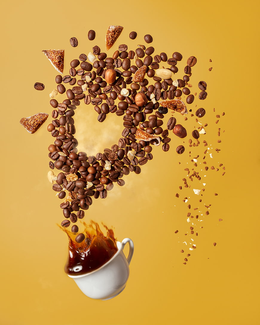 Coffee beans forming heart shape above cup