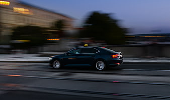 Black taxi speeding on city street at dusk