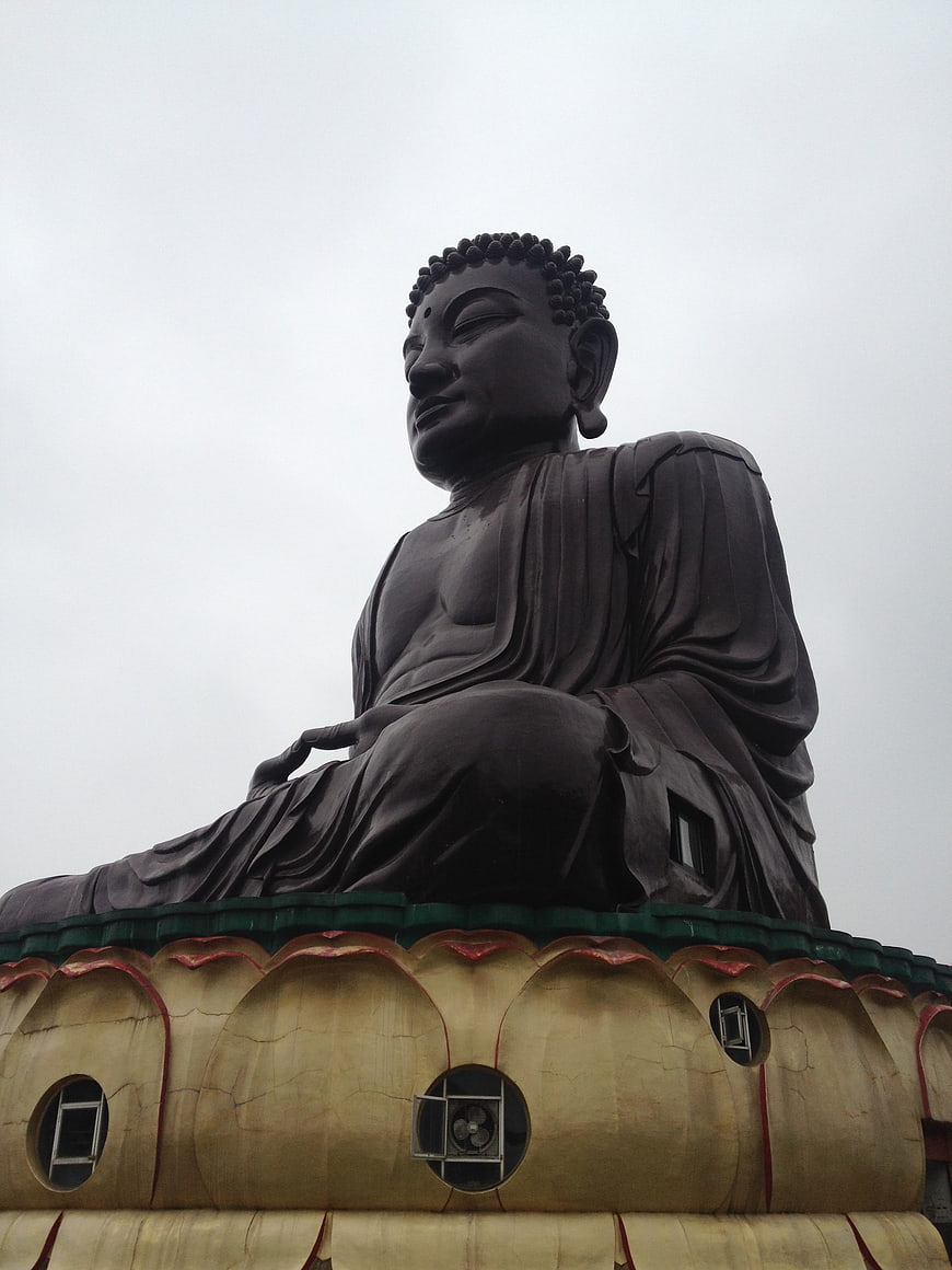 Low angle view of a large dark bronze Buddha statue on a golden lotus base