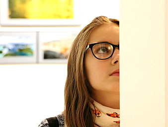 Woman with glasses peeking around a corner in gallery