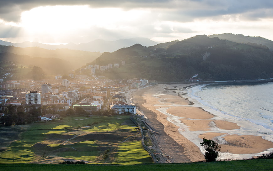 Sunlit coastal cityscape with golf course and sandy beach