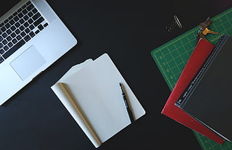Flat lay of laptop, notebook, and books on dark desk