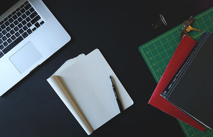 Flat lay of laptop, notebook, and books on dark desk